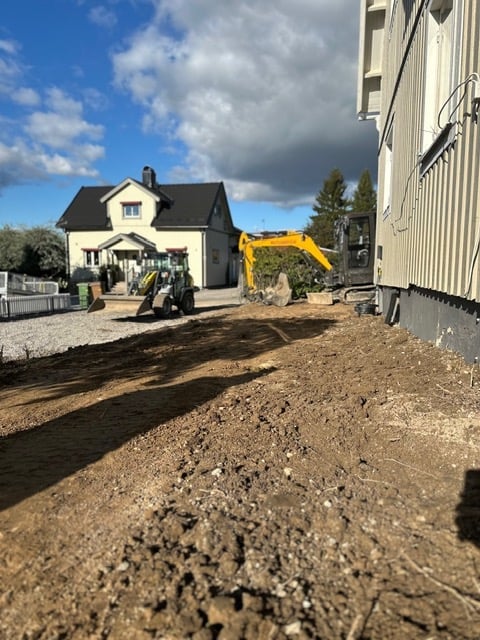 Construction site with yellow excavator, white house, and large metal building under development on sunny day